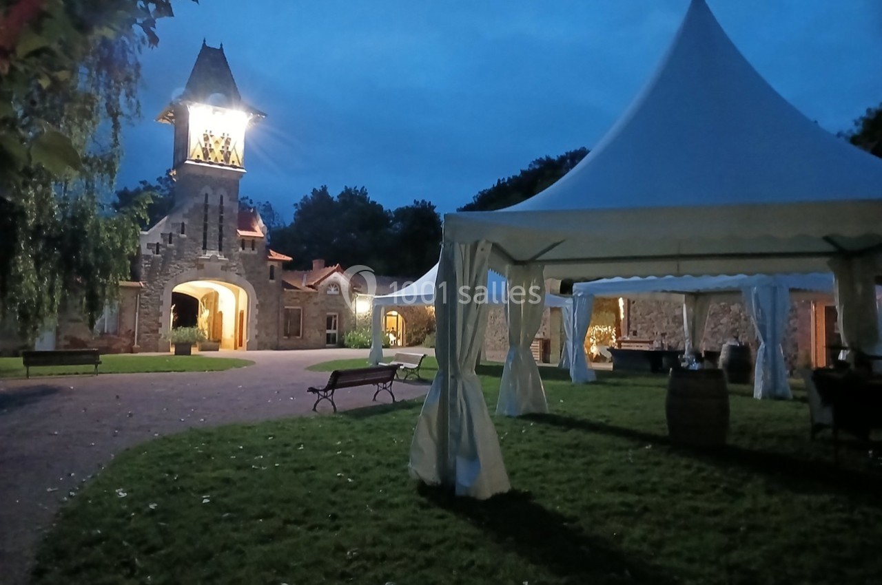Cour extérieure éclairée au crépuscule avec des tentes blanches et un bâtiment en pierre surmonté d'une tour.