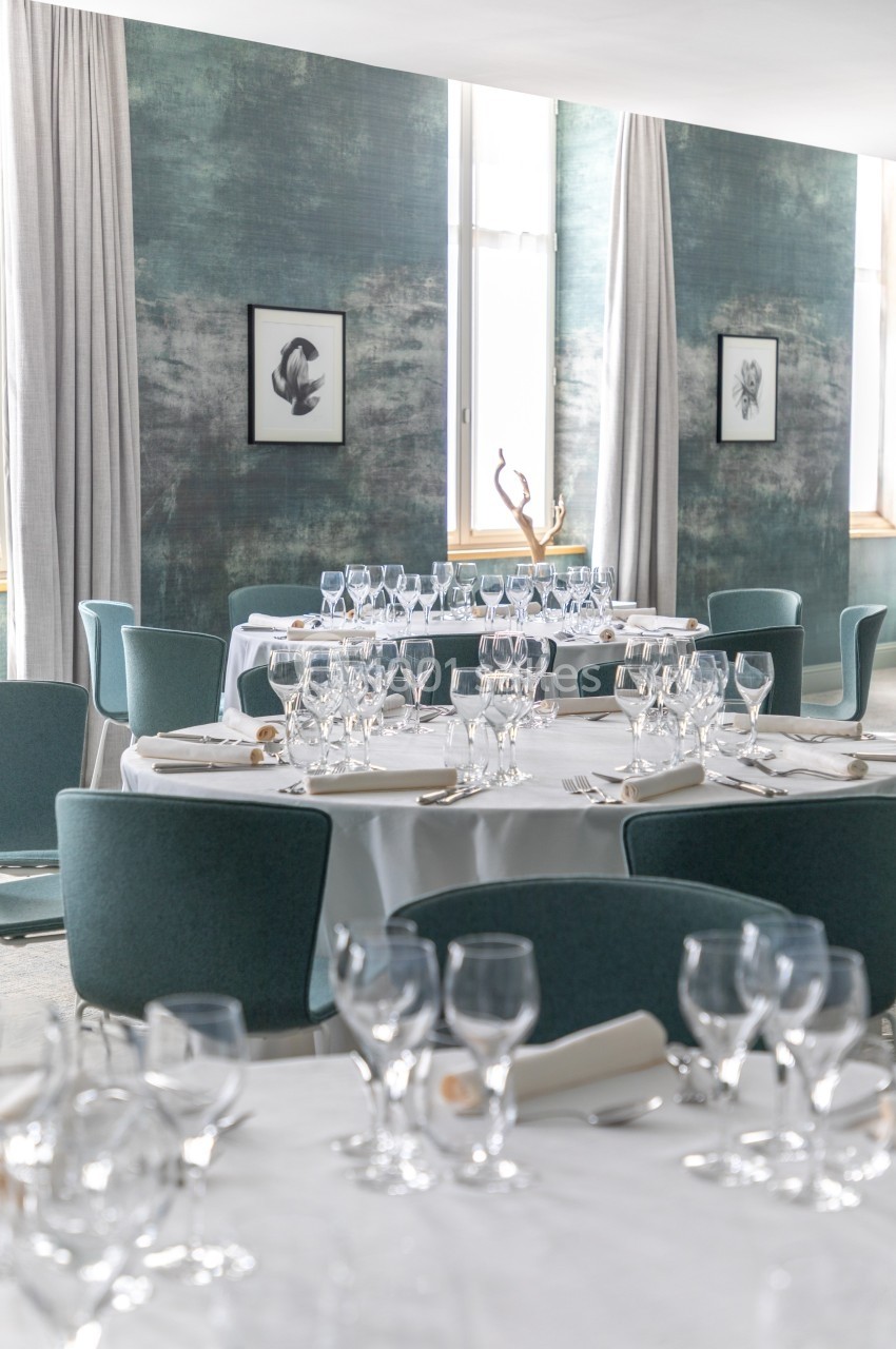 Salle de restaurant élégante avec tables dressées, nappes blanches, verres et couverts, décor mural vert et tableaux…