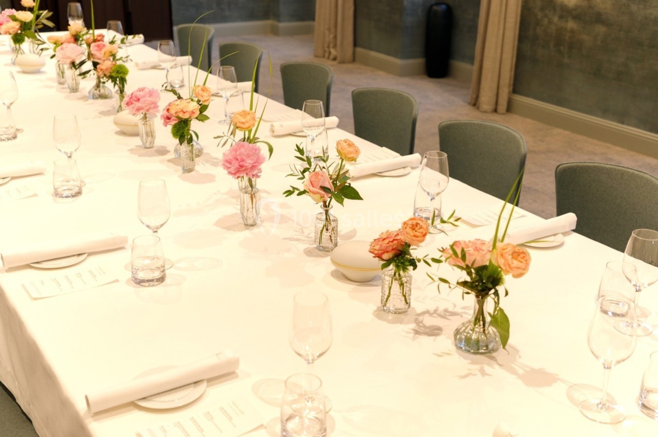 Table dressée avec une nappe blanche, décorée de petits bouquets de fleurs colorées et de verres disposés pour un repas.