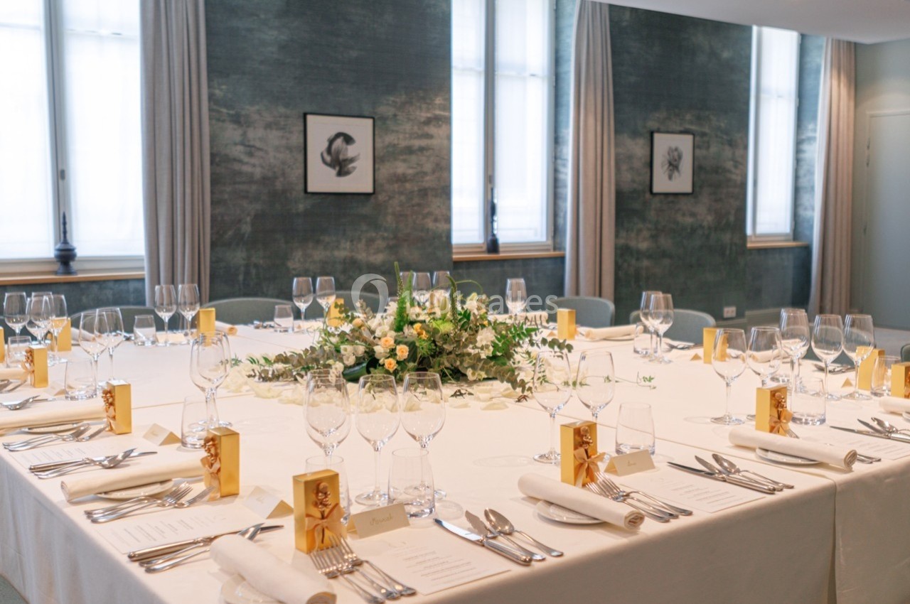 Salle élégante avec tables dressées, nappes blanches, verres, serviettes pliées et centre de table floral.