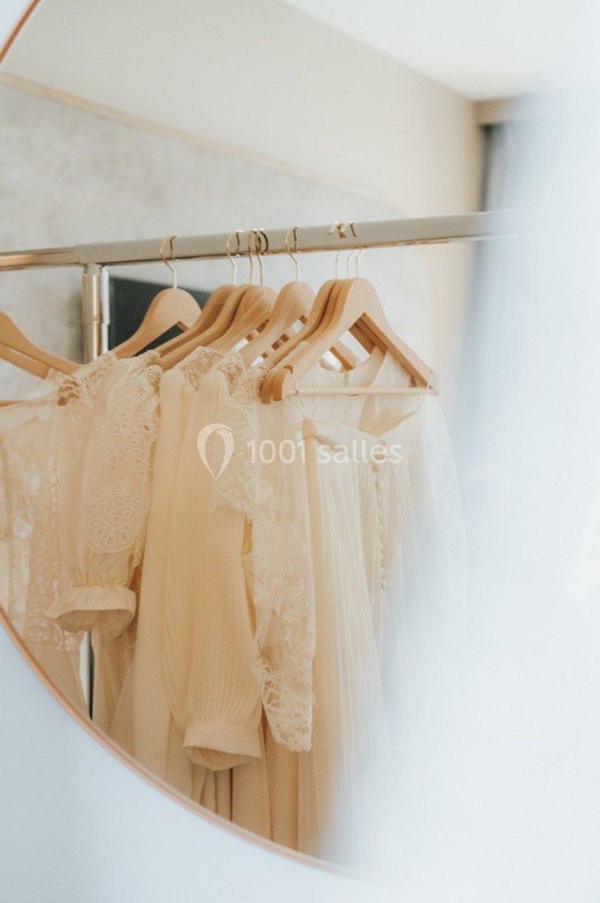 Vêtements blancs délicats en dentelle suspendus à des cintres, reflétés dans un miroir rond.