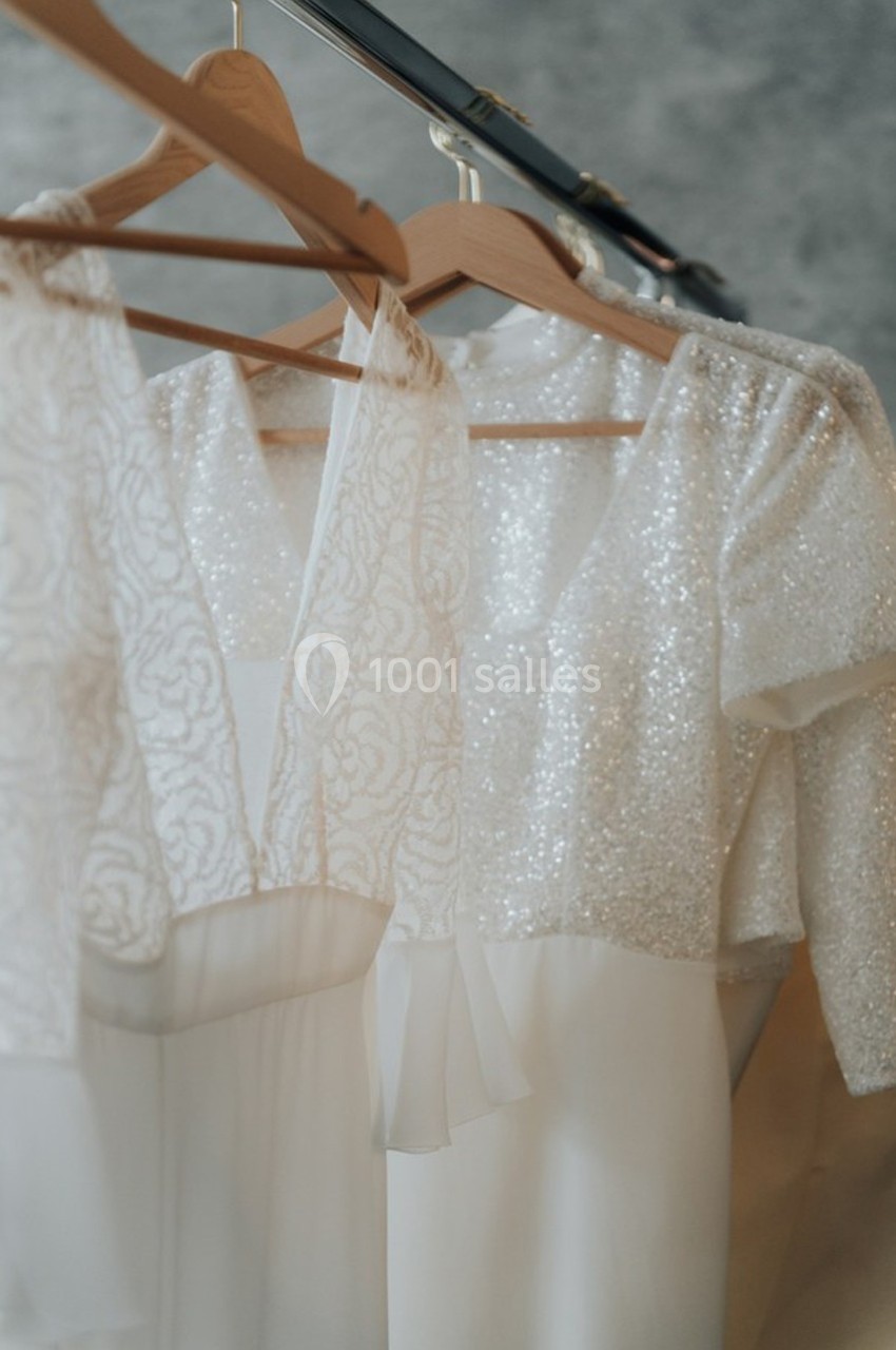 Robes blanches élégantes avec détails en dentelle et paillettes suspendues sur des cintres en bois.