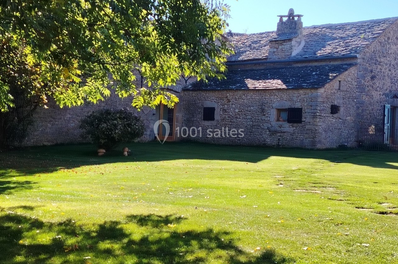 Maison en pierre avec toit en ardoise, entourée d'un jardin verdoyant sous un ciel ensoleillé.