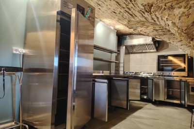 Maison en pierre traditionnelle avec toit en lauze, entourée d'une cour pavée et d'arbres dénudés en hiver.