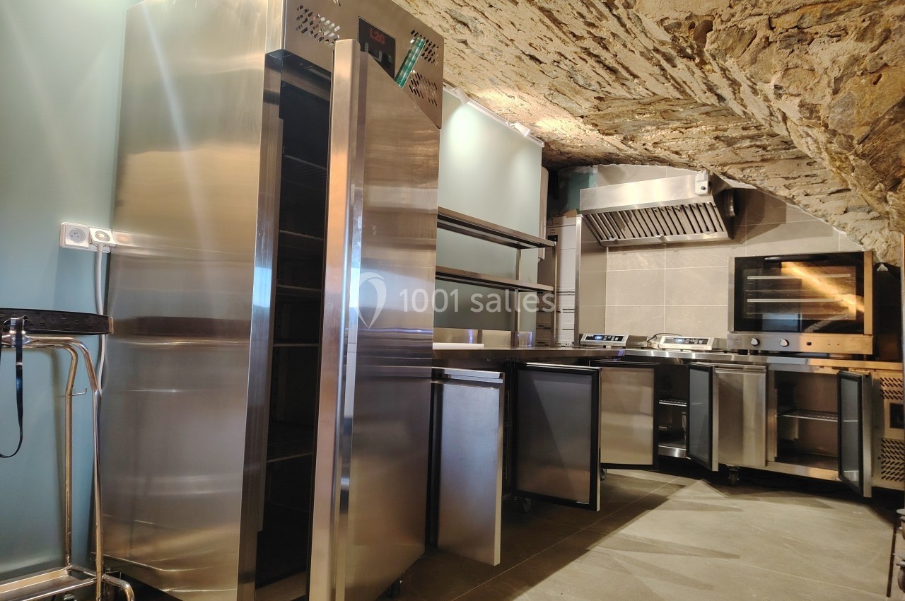 Cuisine professionnelle moderne avec équipements en inox sous un plafond voûté en pierre apparente.