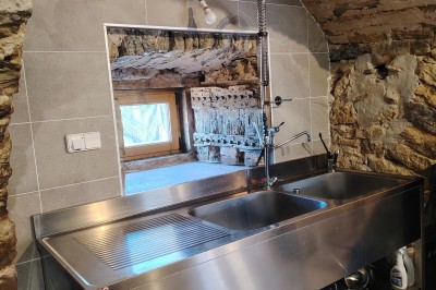 Maison en pierre traditionnelle avec toit en lauze, entourée d'une cour pavée et d'arbres dénudés en hiver.