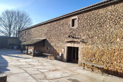 Maison en pierre traditionnelle avec toit en lauze, entourée d'une cour pavée et d'arbres dénudés en hiver.