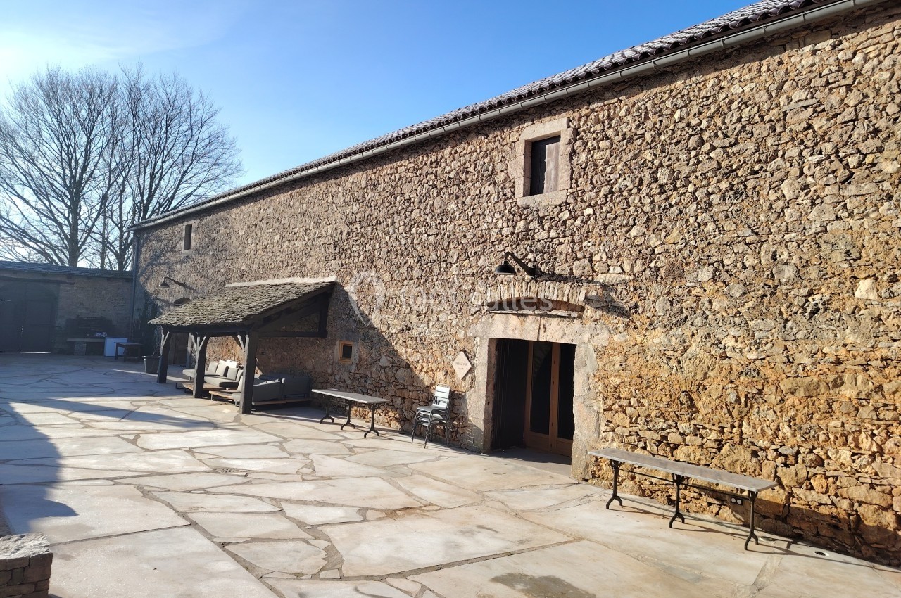 Cour pavée avec un bâtiment en pierre, des bancs en bois et un ciel dégagé en arrière-plan.