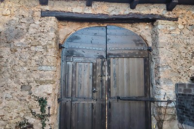 Maison en pierre traditionnelle avec toit en lauze, entourée d'une cour pavée et d'arbres dénudés en hiver.