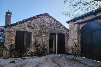Maison en pierre traditionnelle avec toit en lauze, entourée d'une cour pavée et d'arbres dénudés en hiver.