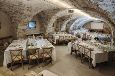 Salle voûtée en pierre avec une table ronde dressée, ornée de fleurs blanches et serviettes pliées bleues.