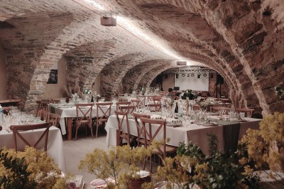 Salle voûtée en pierre avec une table ronde dressée, ornée de fleurs blanches et serviettes pliées bleues.