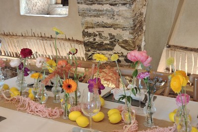 Salle voûtée en pierre avec une table ronde dressée, ornée de fleurs blanches et serviettes pliées bleues.