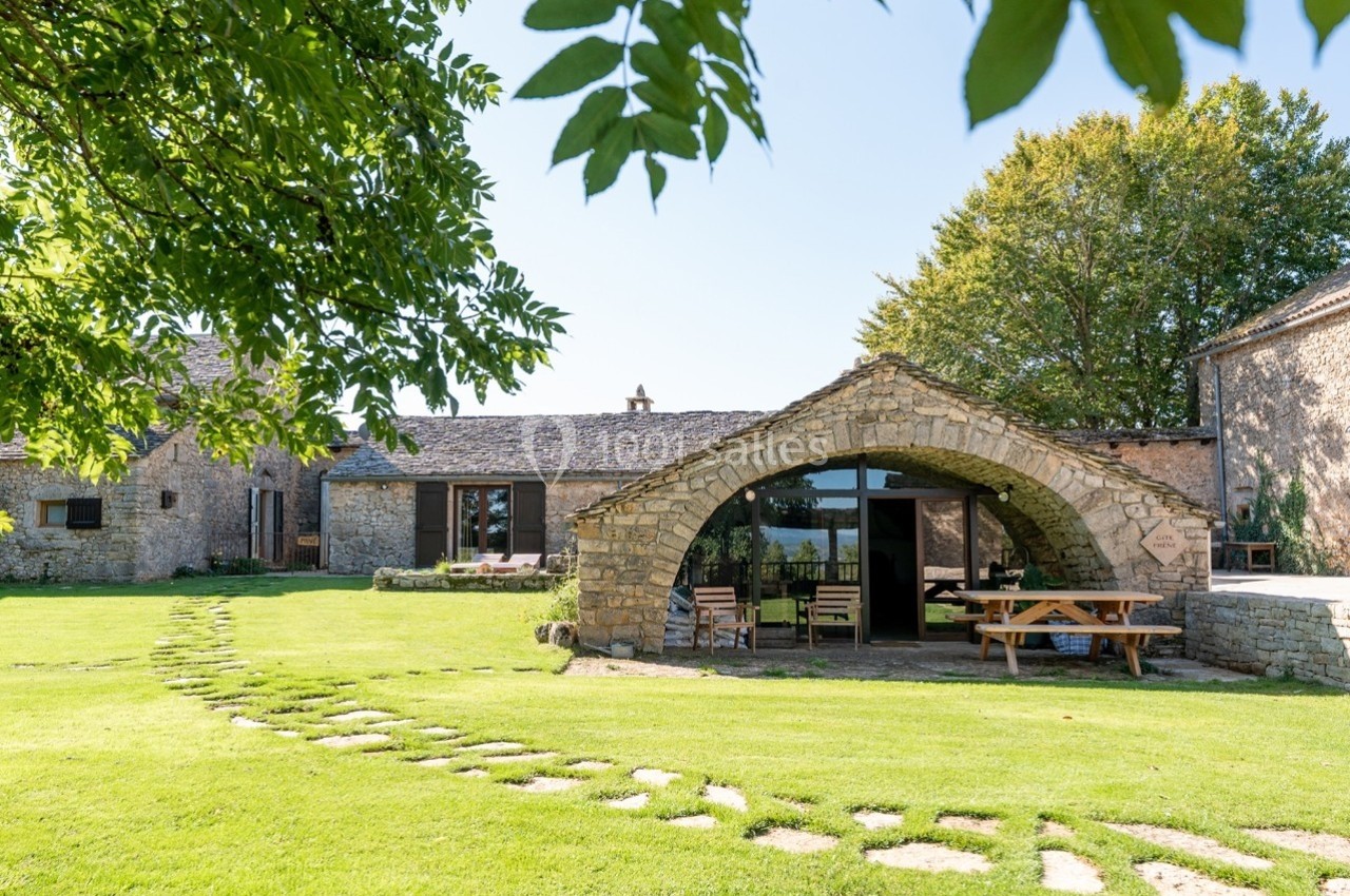Bâtisse en pierre avec arche, entourée de pelouse et d'arbres, sous un ciel dégagé.