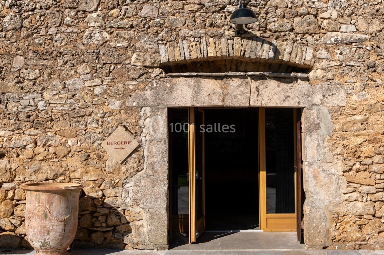 Entrée d'une bergerie en pierre avec une porte en bois ouverte et un pot en terre cuite à gauche.