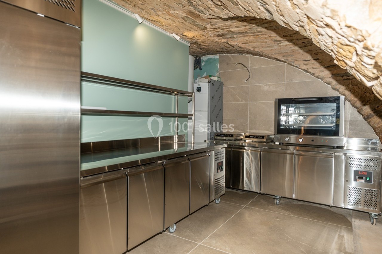 Cuisine professionnelle sous une voûte en pierre, équipée de meubles en inox, d'un four et d'appareils de cuisson modernes.