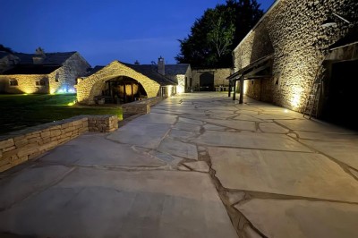 Chambre avec murs en pierre, lit double avec couverture blanche et cheminée ancienne en pierre.