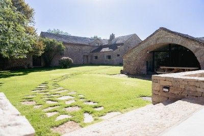 Chambre avec murs en pierre, lit double avec couverture blanche et cheminée ancienne en pierre.