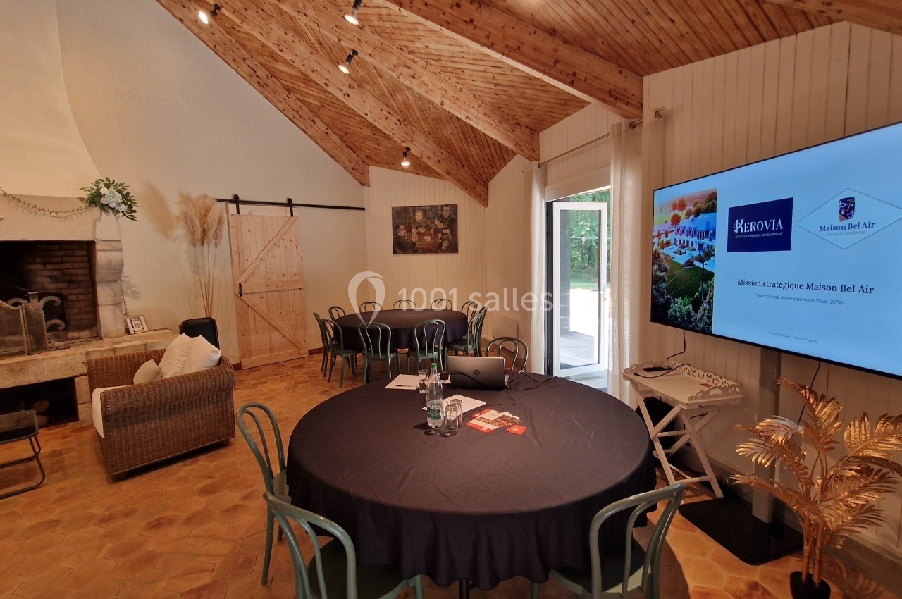 Salle de réunion avec tables rondes, cheminée, écran affichant une présentation et décoration intérieure chaleureuse.