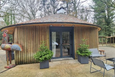 Espace extérieur avec tables hautes dressées et une cabane en bois, entouré d'arbres dans un cadre naturel.
