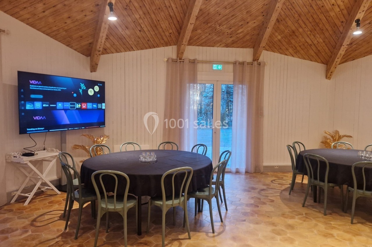 Salle de réunion avec tables rondes, chaises, écran mural allumé et plafond en bois sous éclairage chaleureux.