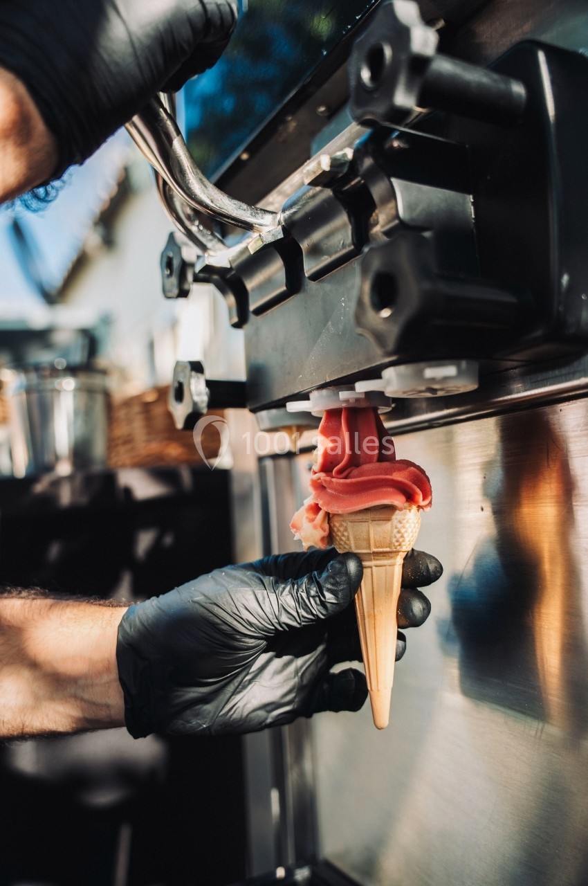 Une main gantée tenant un cornet de glace rempli à une machine à glace automatique en extérieur.