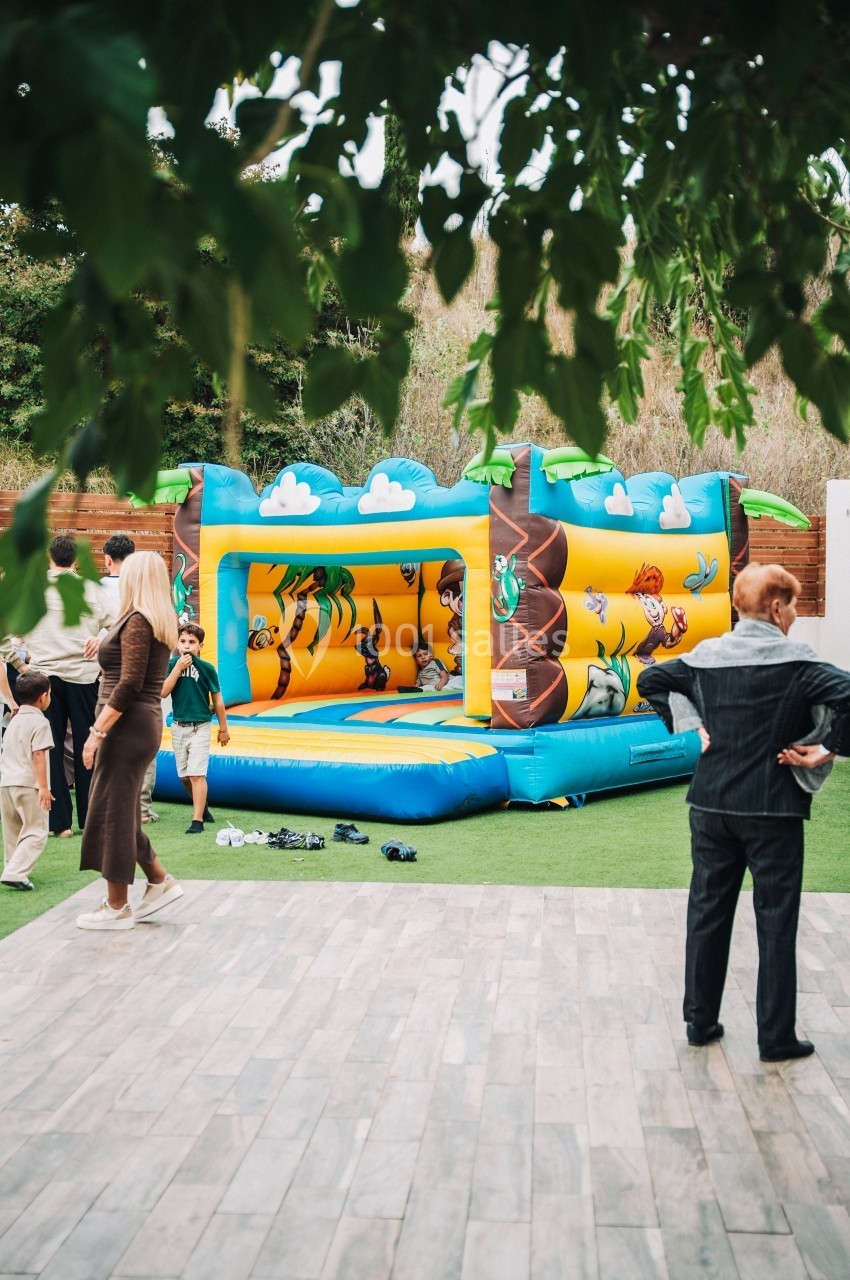 Structure gonflable colorée sur le thème de la jungle dans un jardin, entourée de personnes.
