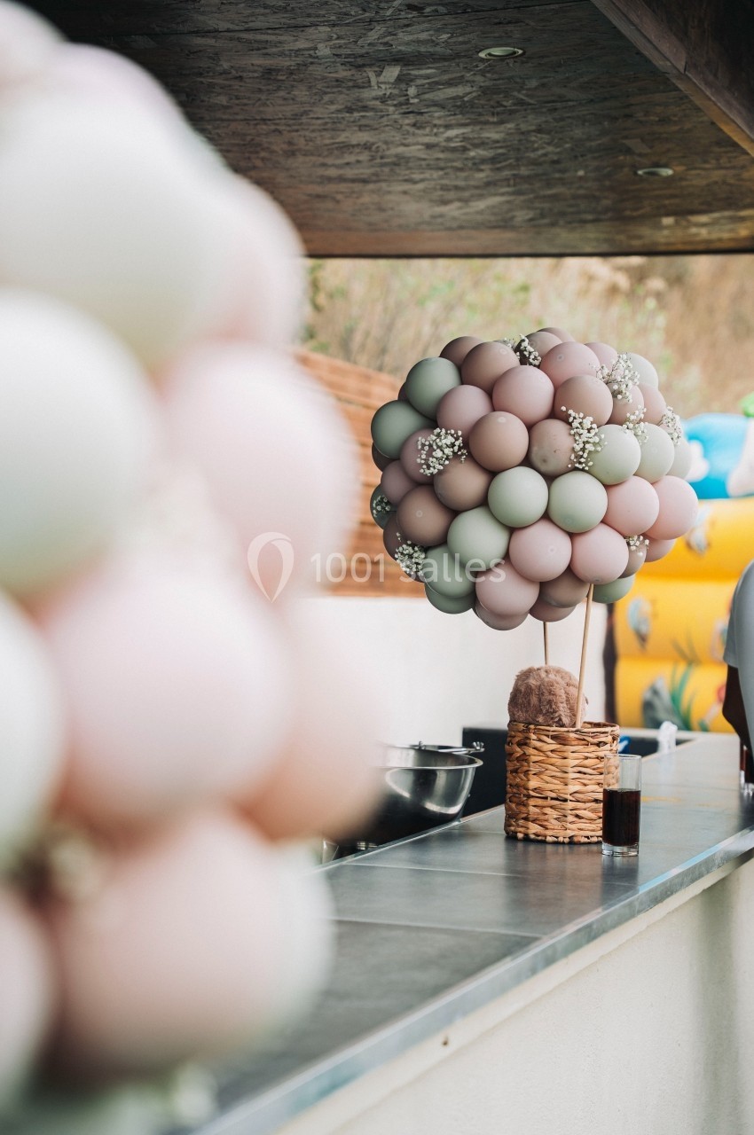 Bouquet de ballons pastel décoratif sur un comptoir extérieur, avec des éléments de fête en arrière-plan.