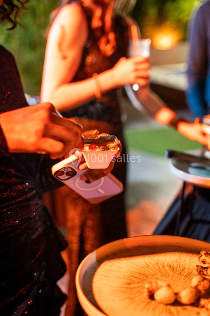 Personnes en tenue de soirée dégustant des amuse-bouches lors d'un événement en extérieur, ambiance chaleureuse.