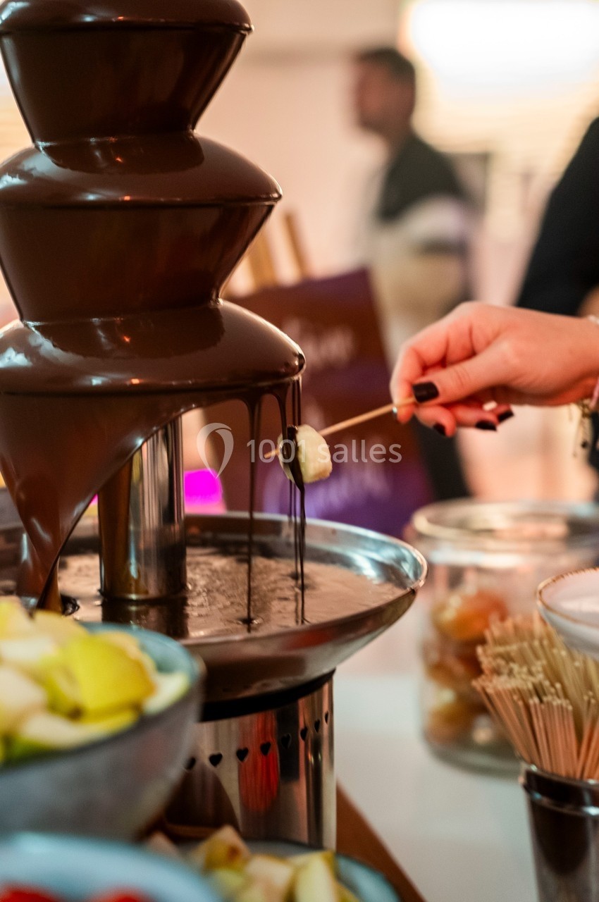 Fontaine de chocolat avec une personne trempant un morceau de fruit sur une brochette.