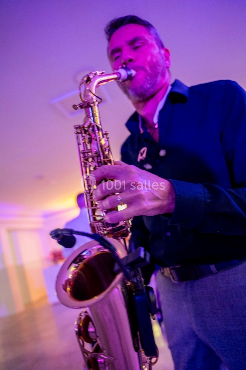 Un homme joue du saxophone dans une ambiance lumineuse violette et jaune.