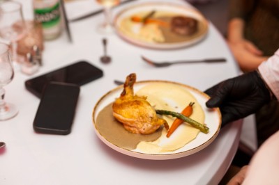 Salle de réception spacieuse avec tables rondes dressées, chaises blanches et éclairage doux.