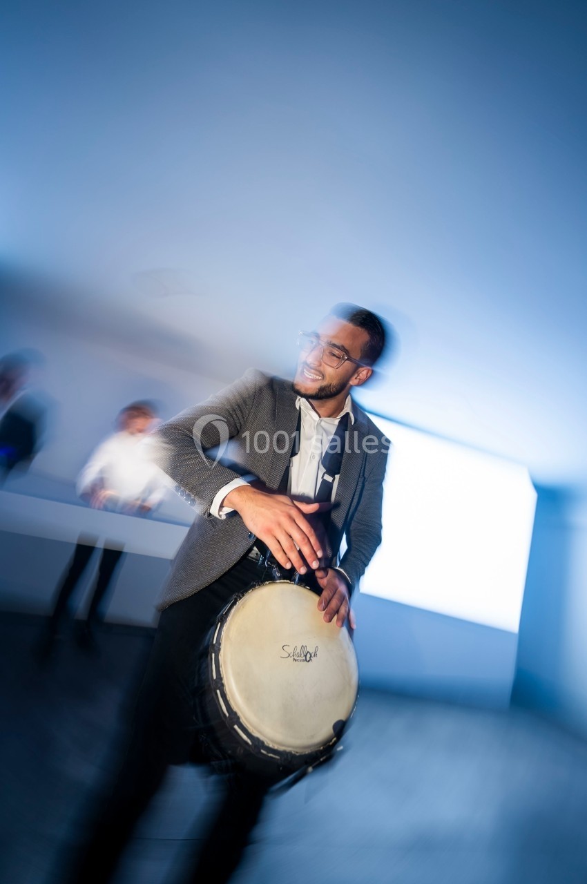 Un homme en costume joue du tambour dans une pièce lumineuse avec un arrière-plan flou.