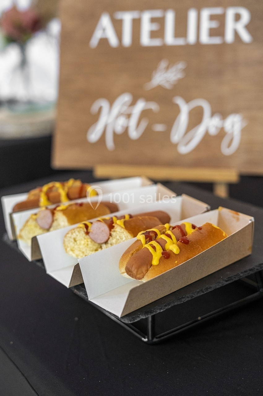 Trois hot-dogs garnis de moutarde et ketchup, présentés dans des barquettes en carton sur une table noire.