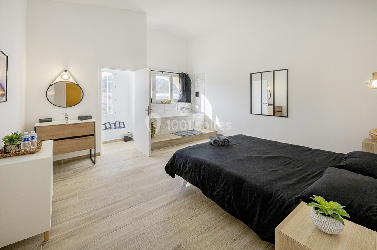 Chambre lumineuse avec lit double, sol en bois clair, salle de bain attenante et décoration minimaliste.