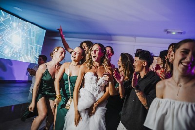 Salle de réception spacieuse avec tables rondes dressées, chaises blanches et éclairage doux.