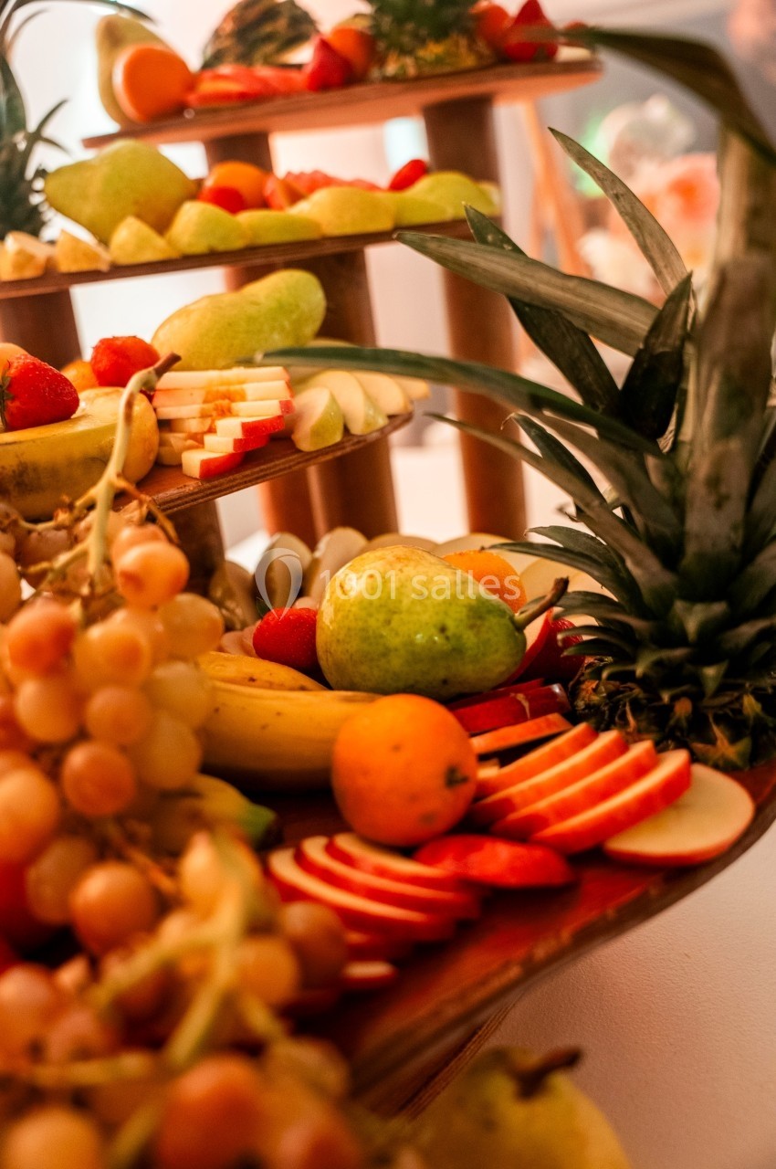 Plateau de fruits variés avec ananas, raisins, pommes tranchées, poires, bananes et agrumes disposés sur plusieurs niveaux.