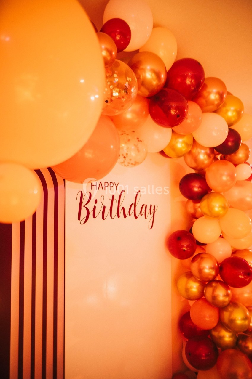 Décoration murale avec des ballons rouges, dorés et blancs entourant un message ’Happy Birthday’ sur fond clair.