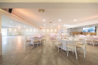 Salle de réception spacieuse avec tables rondes dressées, chaises blanches et éclairage doux.