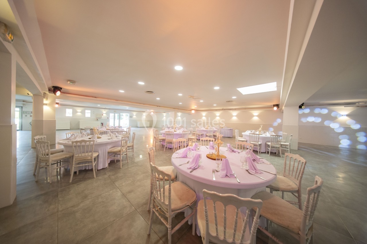 Salle de réception lumineuse avec tables rondes dressées, nappes blanches et chaises en bois clair.