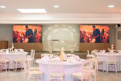 Salle de réception spacieuse avec tables rondes dressées, chaises blanches et éclairage doux.