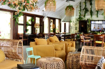 Chambre lumineuse avec lit à baldaquin, décoration tropicale, grandes fenêtres ouvertes sur une terrasse verdoyante.