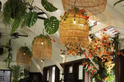 Chambre lumineuse avec lit à baldaquin, décoration tropicale, grandes fenêtres ouvertes sur une terrasse verdoyante.