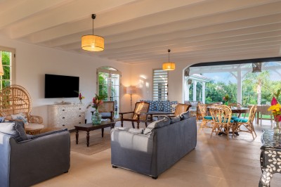 Chambre lumineuse avec lit à baldaquin, décoration tropicale, grandes fenêtres ouvertes sur une terrasse verdoyante.