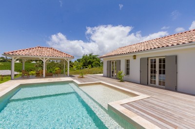 Chambre lumineuse avec lit à baldaquin, décoration tropicale, grandes fenêtres ouvertes sur une terrasse verdoyante.