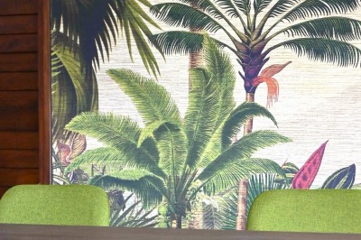 Allée bordée de haies fleuries et de palmiers, menant à une maison sous un ciel bleu.