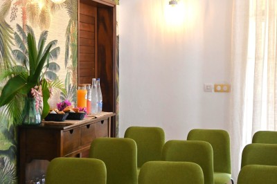 Allée bordée de haies fleuries et de palmiers, menant à une maison sous un ciel bleu.