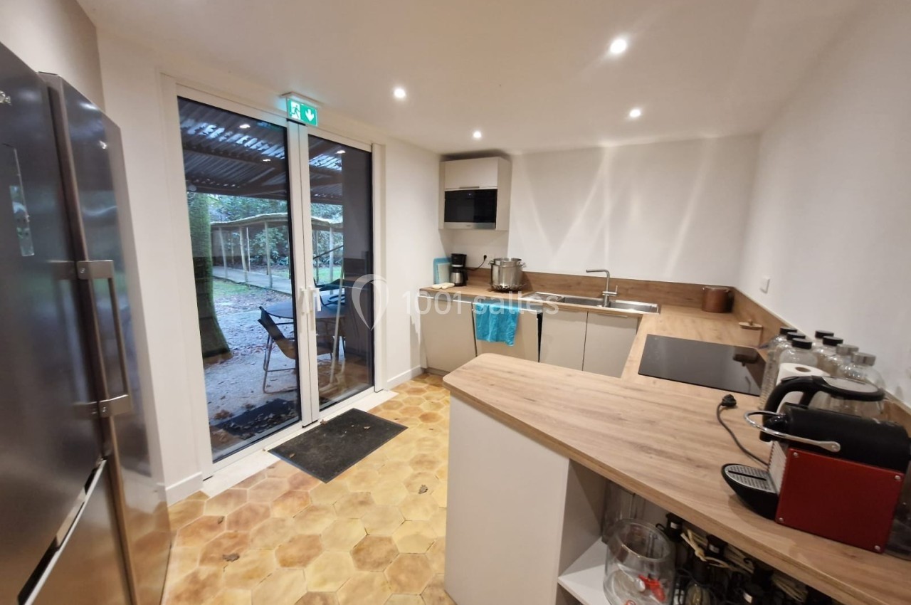 Cuisine moderne avec plan de travail en bois, électroménagers, sol en carrelage hexagonal et porte vitrée donnant sur l…