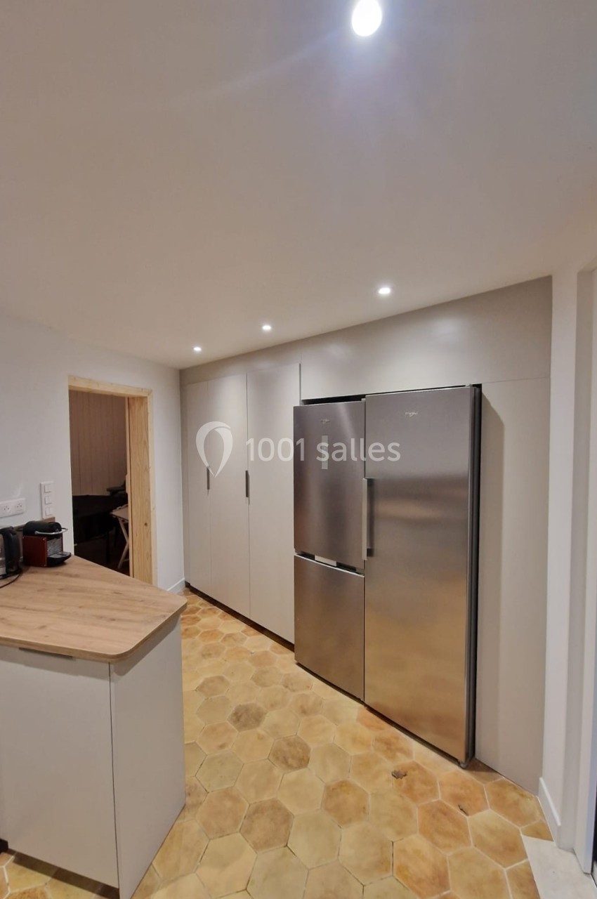 Cuisine moderne avec sol en carreaux hexagonaux, réfrigérateur inox double porte et plan de travail en bois clair.