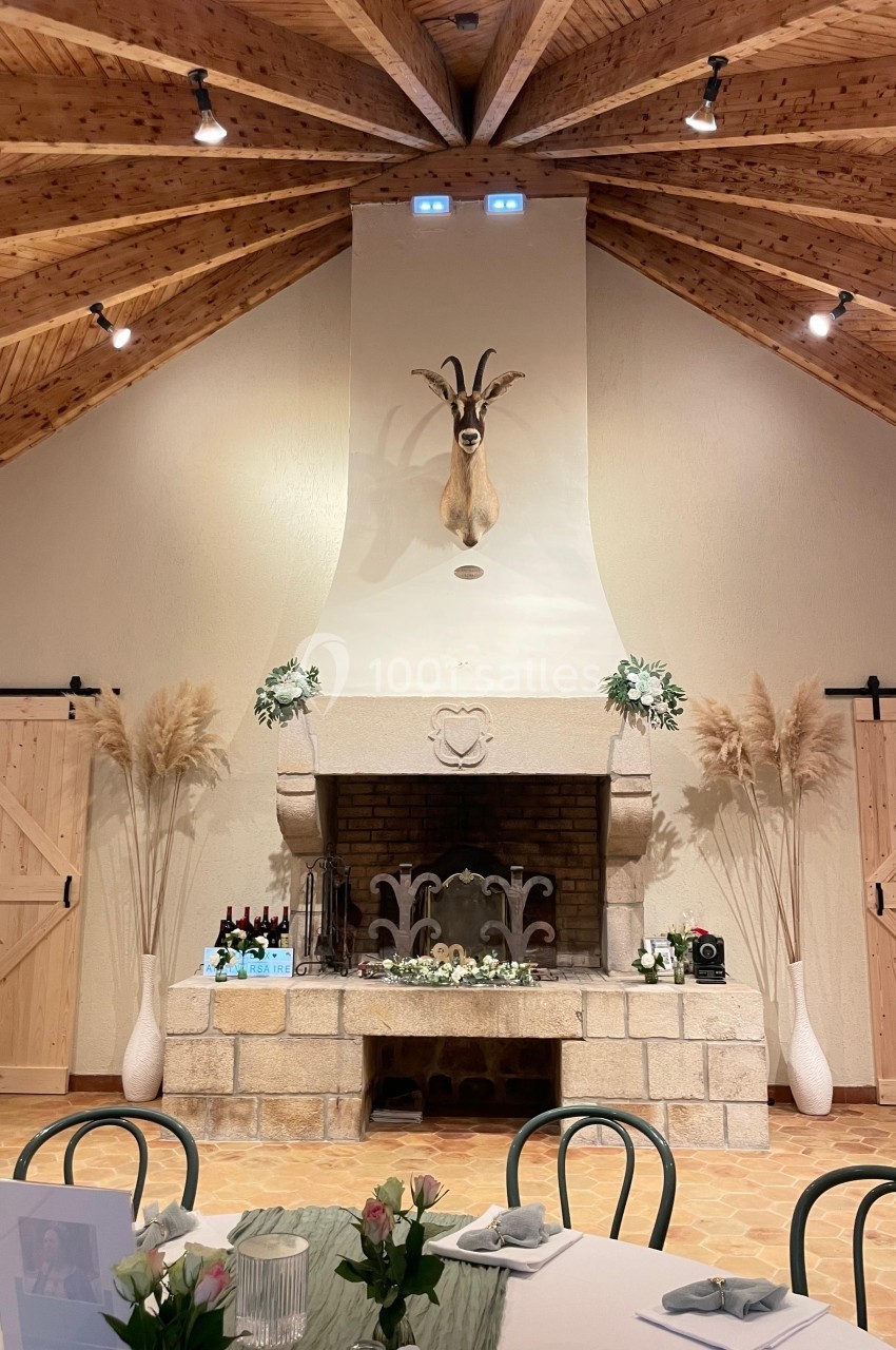 Cheminée en pierre décorée de fleurs, avec une tête de bouquetin au mur, dans une salle au plafond en bois.